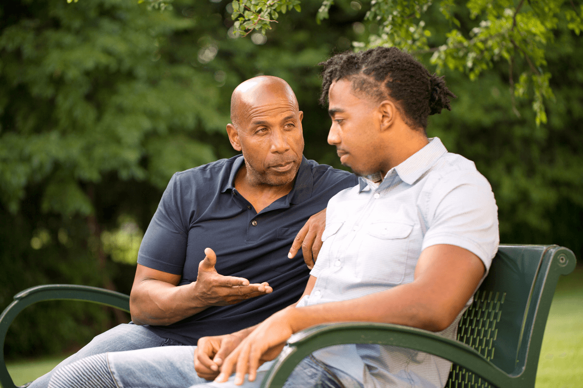 two adult African American men sitting on a bench talking